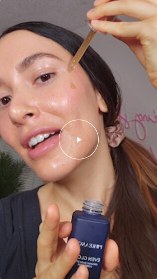 Woman with long dark hair applying Even Glow serum to her face using a dropper